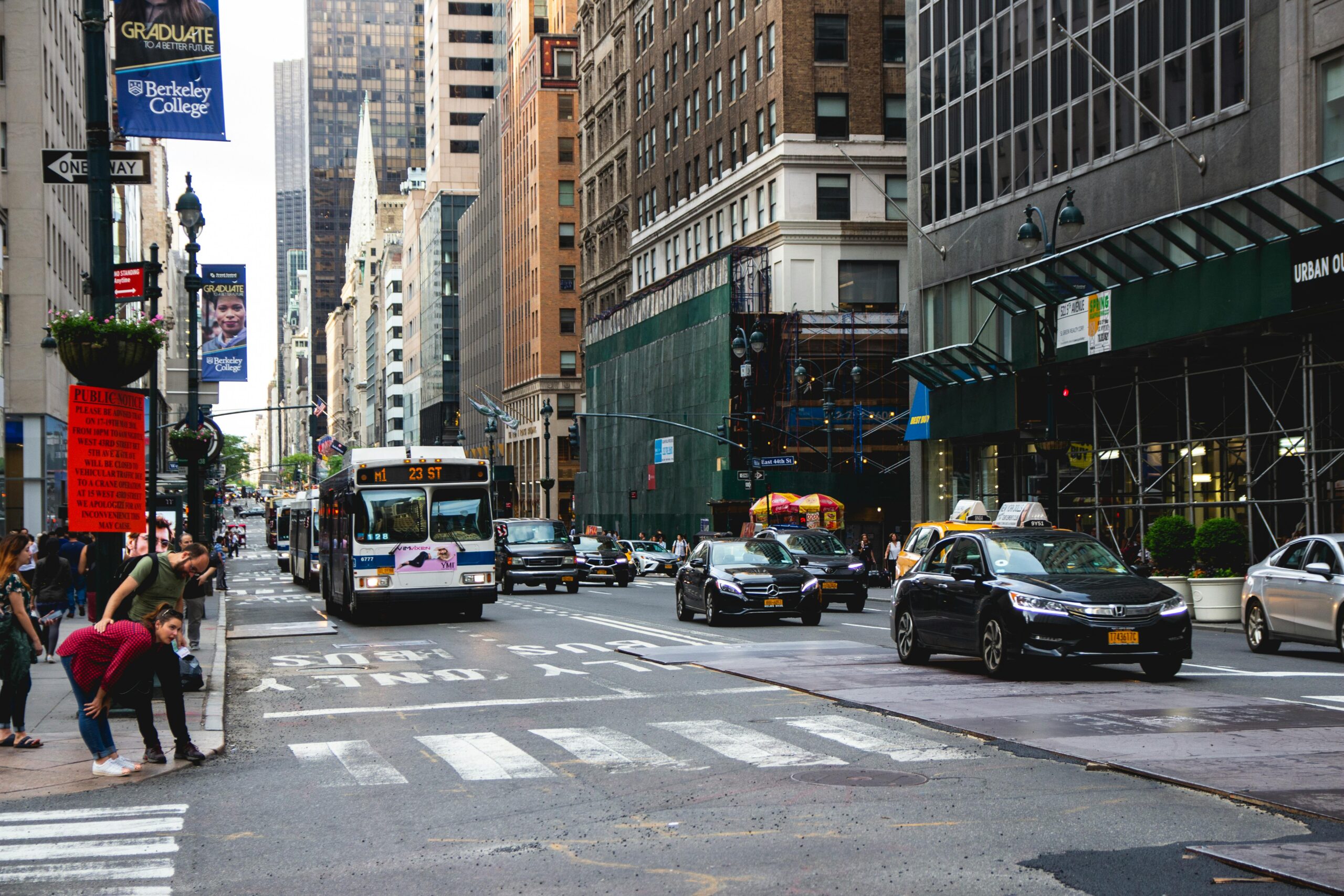 Busy street in New York City with vehicle traffic and pedestrians about to cross the street. 