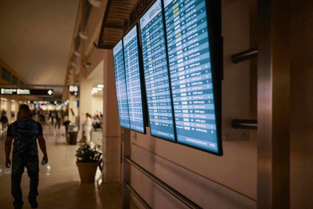 Flight status screens a a busy airport with people walking in the background. 