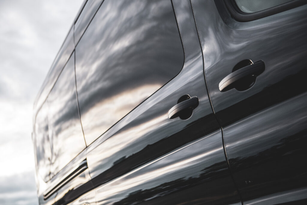 Side of a black Ford Transit rental van with a Greenvans logo on the window