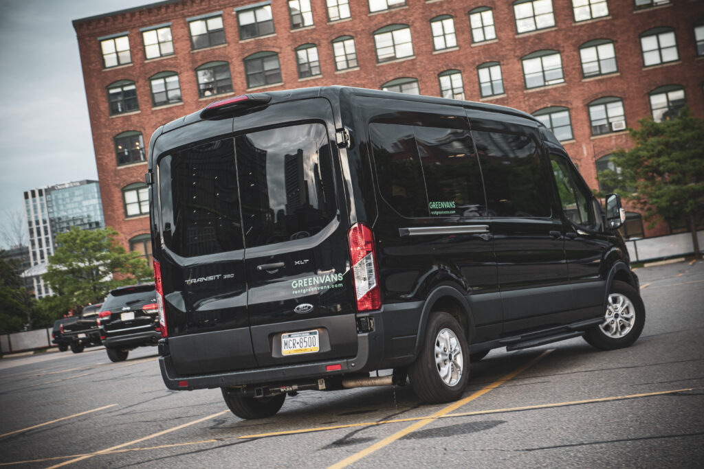 the back of a black Ford Transit passenger van in a parking lot with a brick office building in the background.