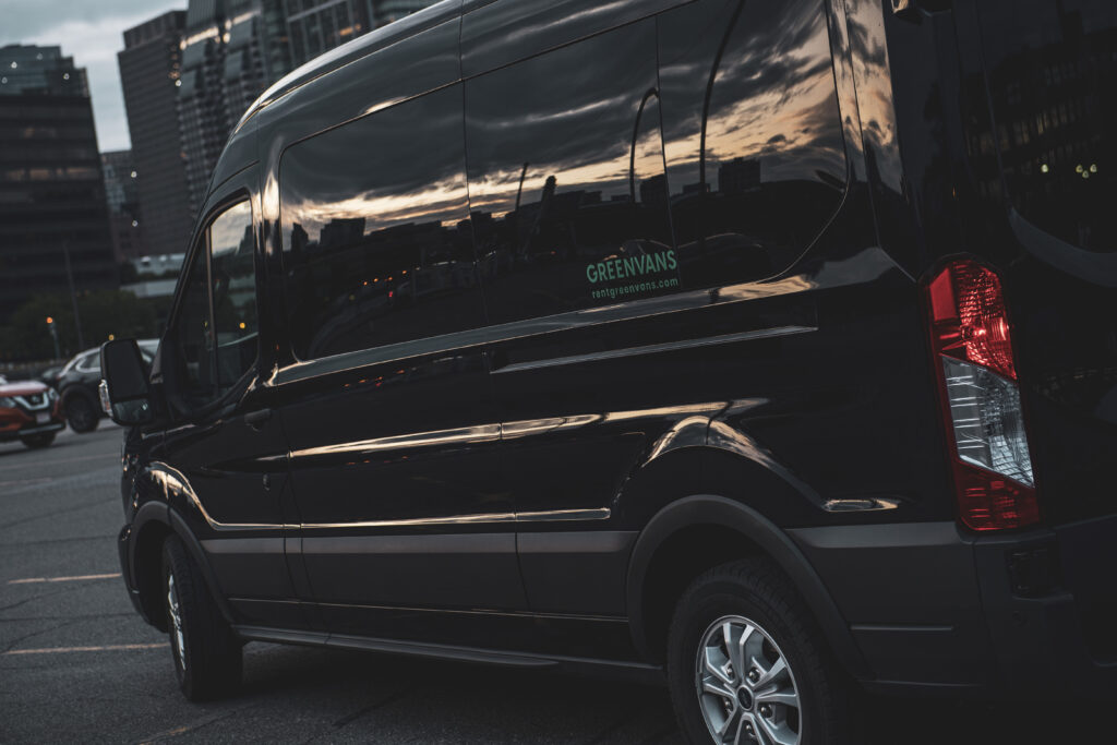 Side of black Black Ford Transit passenger van with Greenvans label