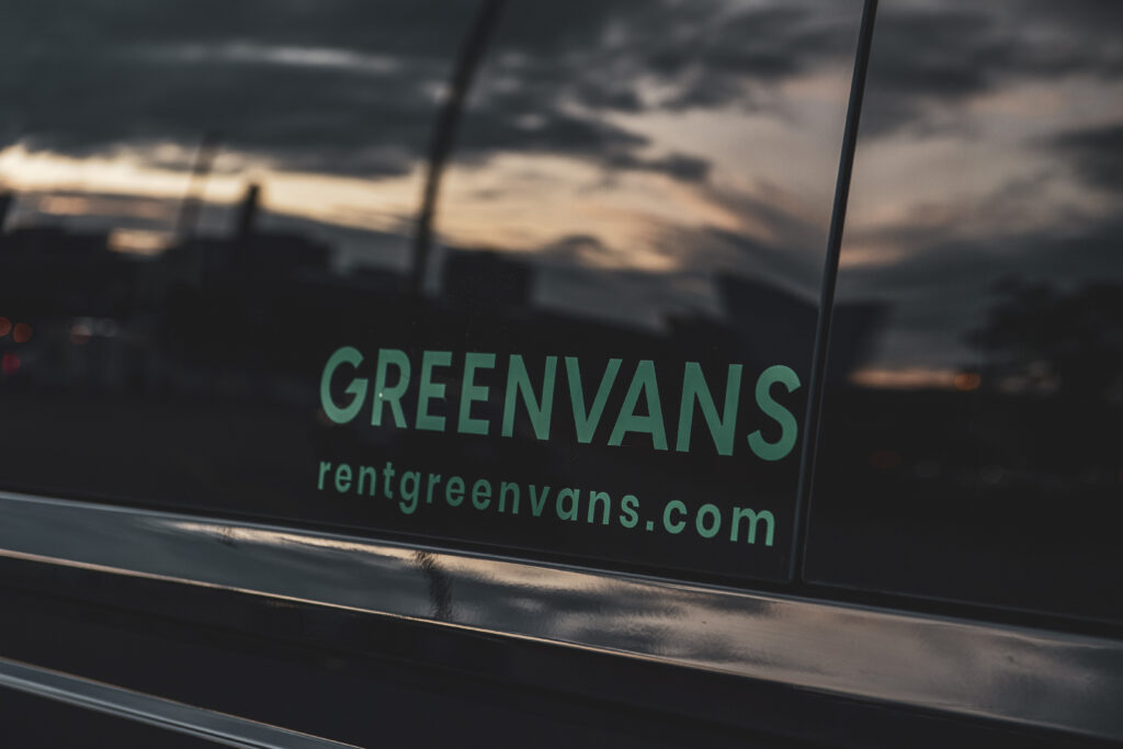 A Greenvans logo on the side of a black Ford Transit passenger van rental