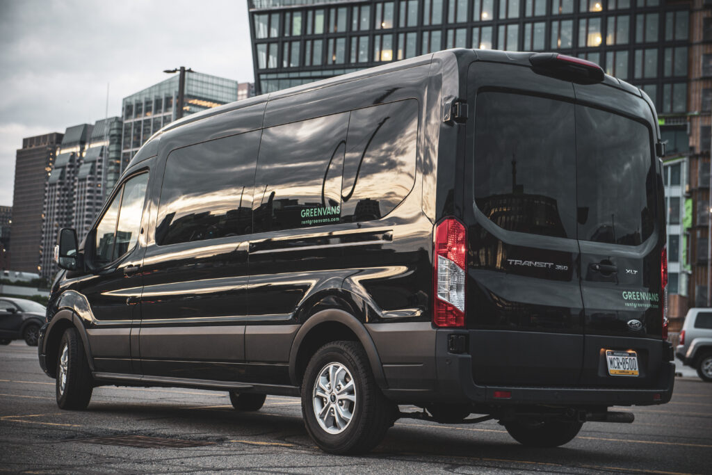 A black ford transit rental van in front of office buildings at dusk.