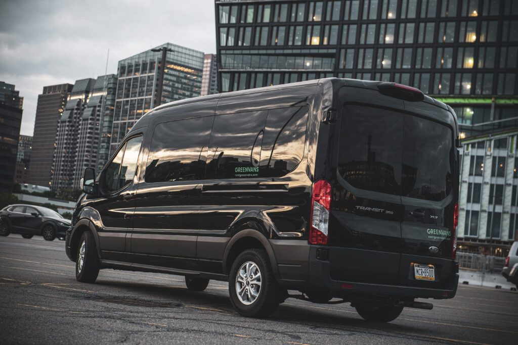 A black Ford Transit passenger van parked in front of office buildings on a cloudy day