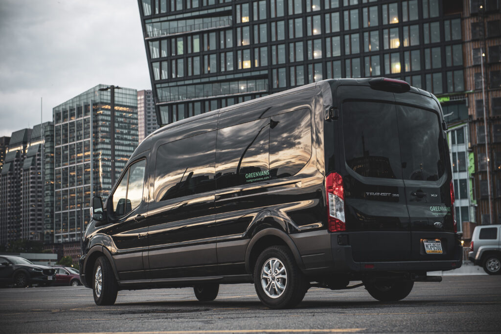 A black Ford Transit passenger van rental in parked front of an office building