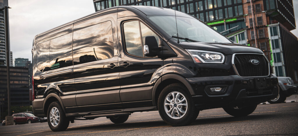 A black Ford Transit passenger van parked in front of a high-rise office building