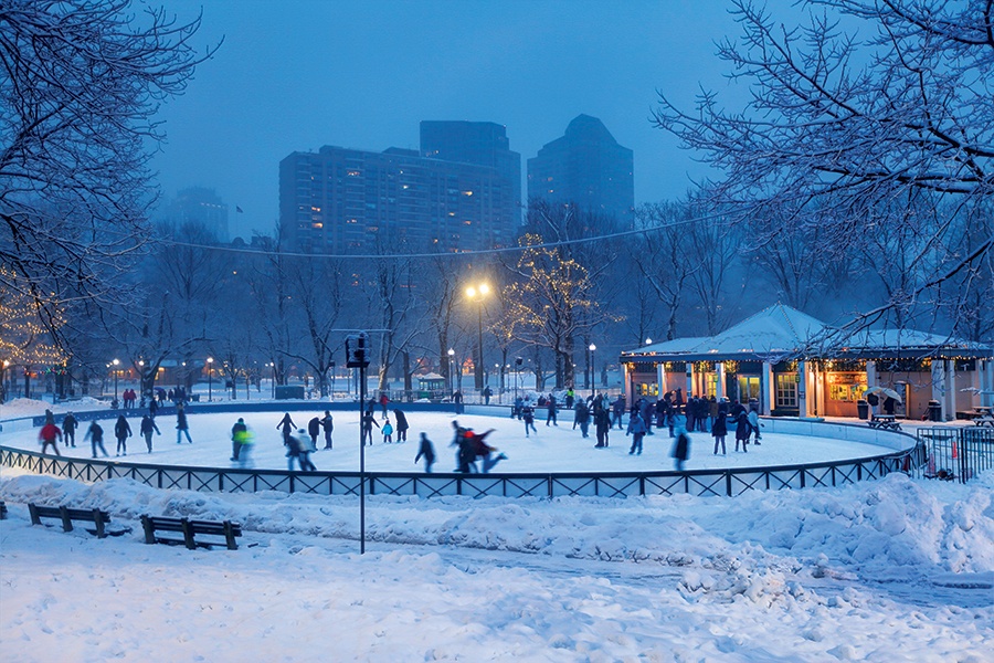 People ice skating on Frog Pond in the snow with Boston skyline in the background