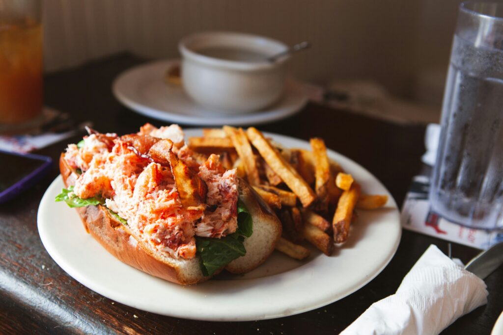 a buttery lobster roll with a side of French fries on a white plate