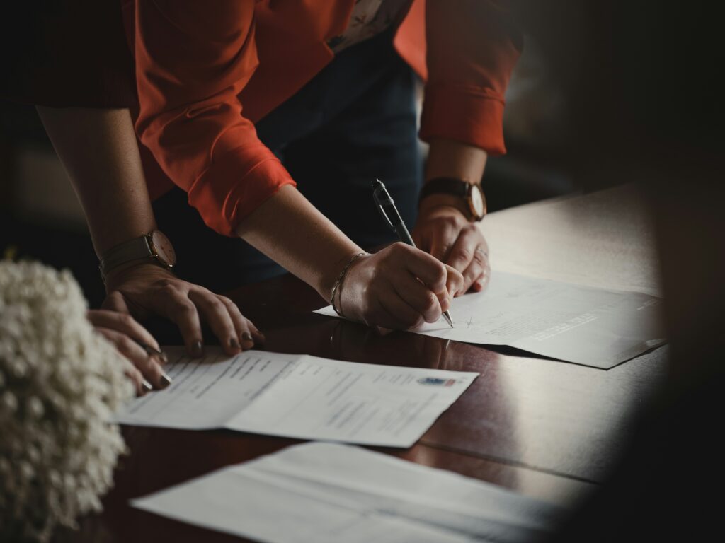 Two people signing paperwork on a wooden table.