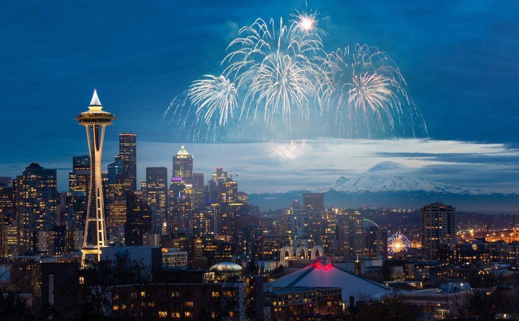 Seattle cityscape at night with fireworks in dark blue sky.